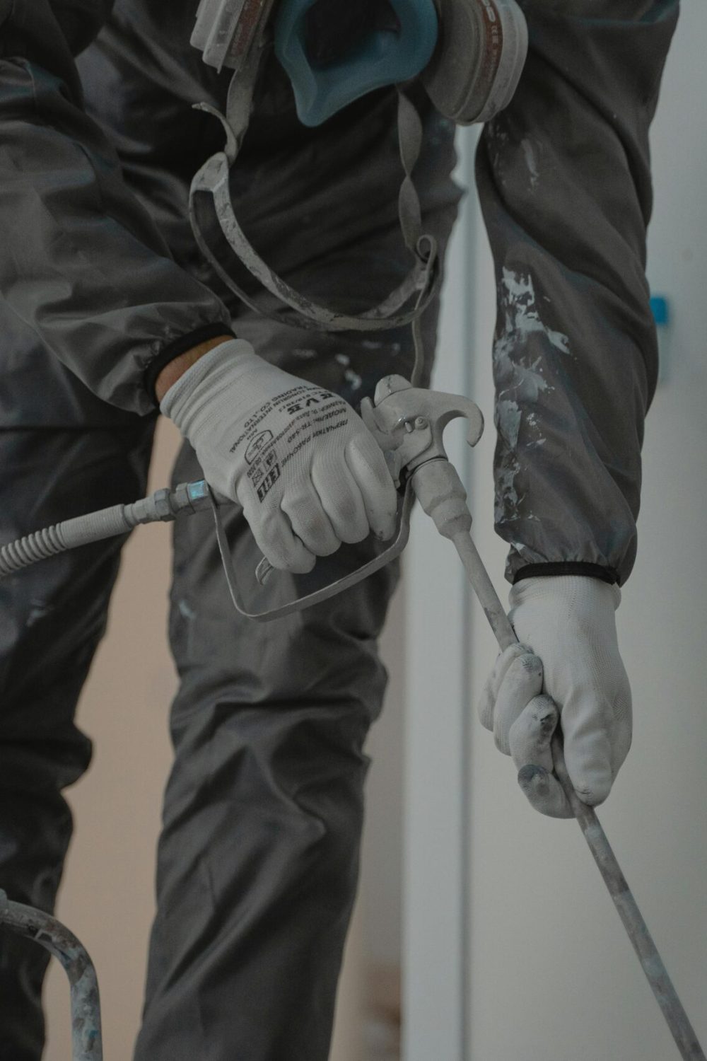 Worker in protective gear using a power spray for indoor renovation.