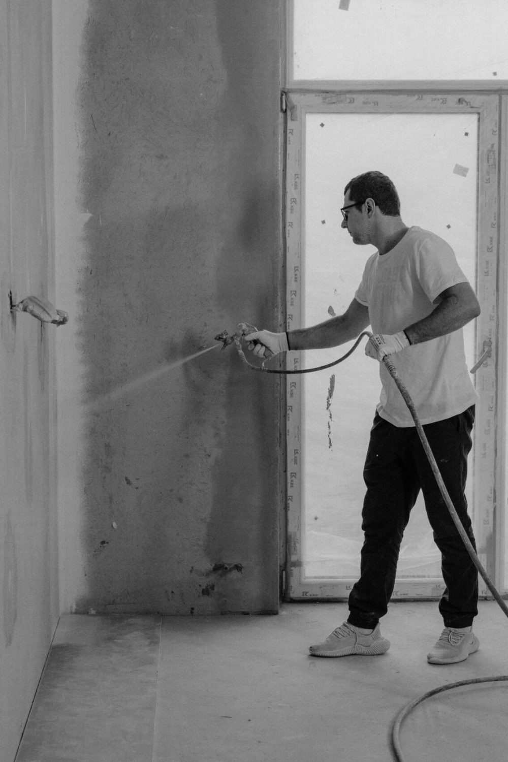 A worker paints an interior wall with a spray gun during a renovation project.